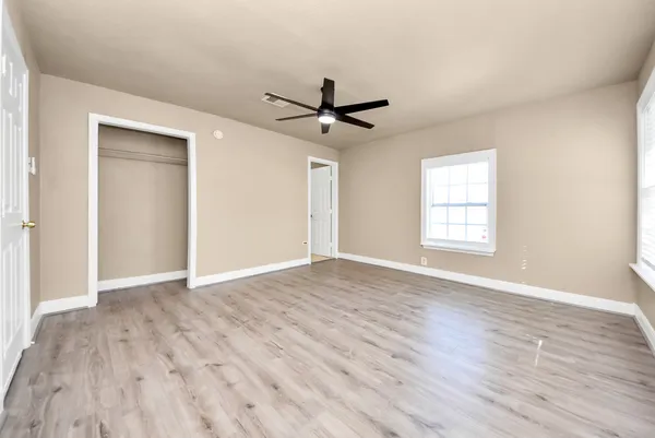 an empty room with wooden floor ceiling fan and windows