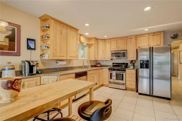 a kitchen with stainless steel appliances granite countertop a sink a stove a refrigerator cabinets and chairs