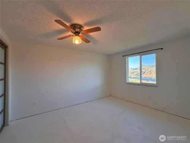an empty room with chandelier fan and windows