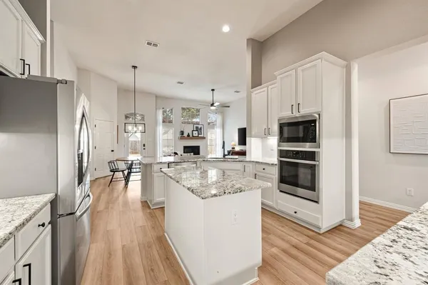 a kitchen with stainless steel appliances a stove a sink a refrigerator and white cabinets with wooden floor