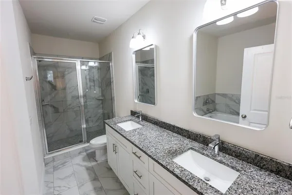 a bathroom with a granite countertop double vanity sink mirror and shower
