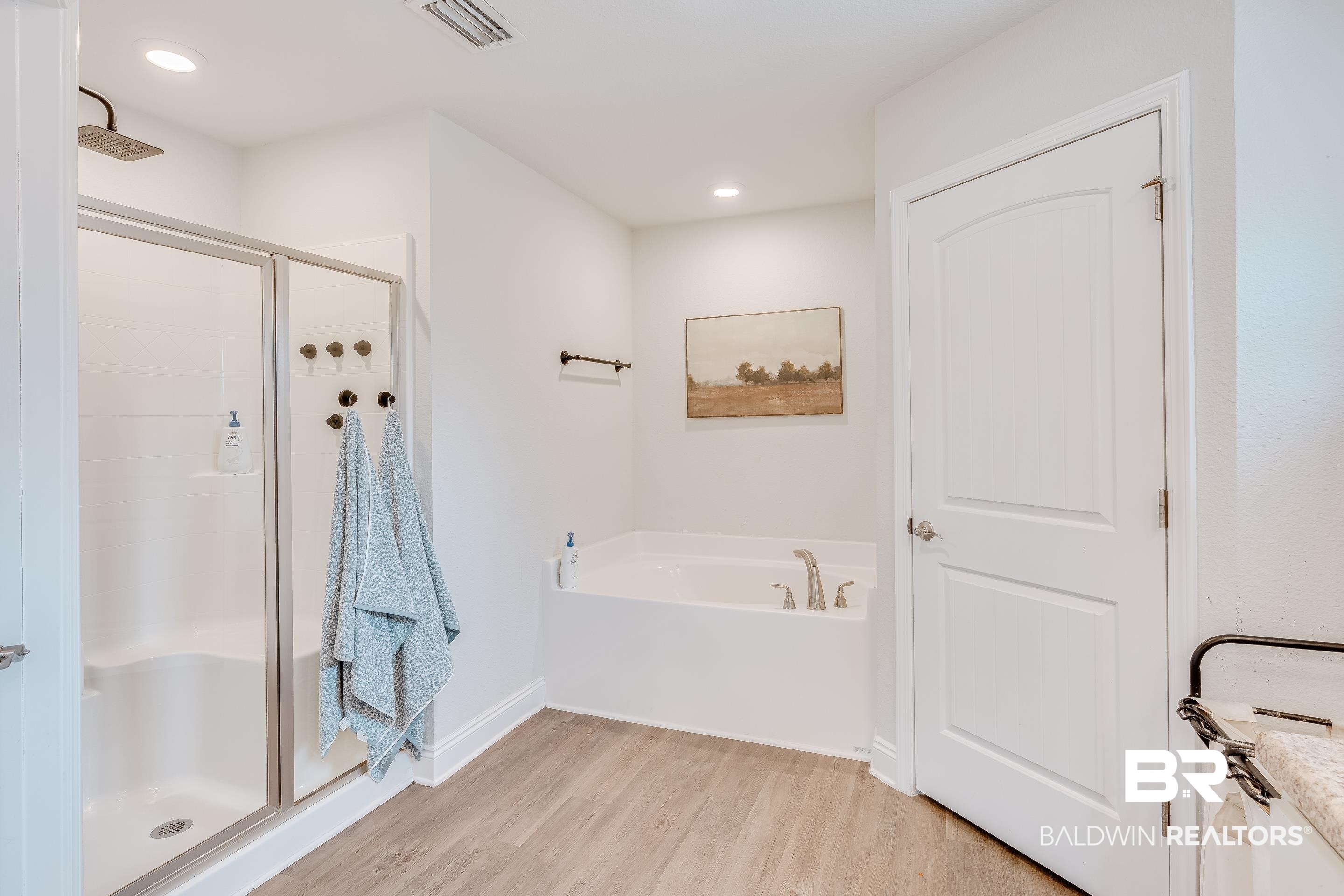 2215 Fernwood Loop West Semmes, AL 36575 - Photo 16 of 40 Contemporary bathroom featuring a glass-enclosed shower with a rainfall showerhead, a built-in soaking tub, wood-finish flooring, recessed lighting, and a white paneled door