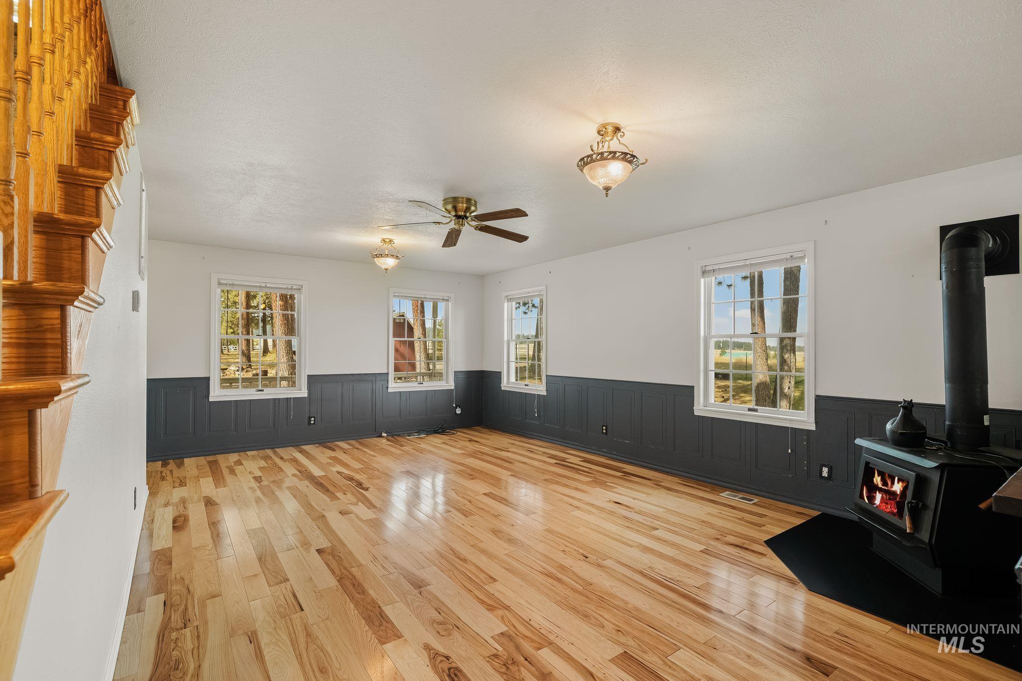 1820 Winchester Road Winchester, ID 83555 - Photo 12 of 50 Hardwood flooring, wood-paneled walls, multiple windows, ceiling fan, and wood-burning stove