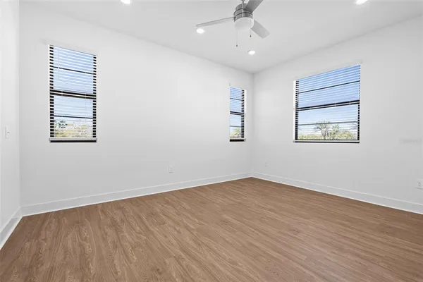 an empty room with wooden floor chandelier fan and windows