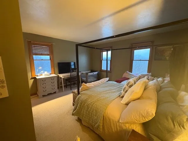 a bedroom with a bed a mirror on the dresser and a window