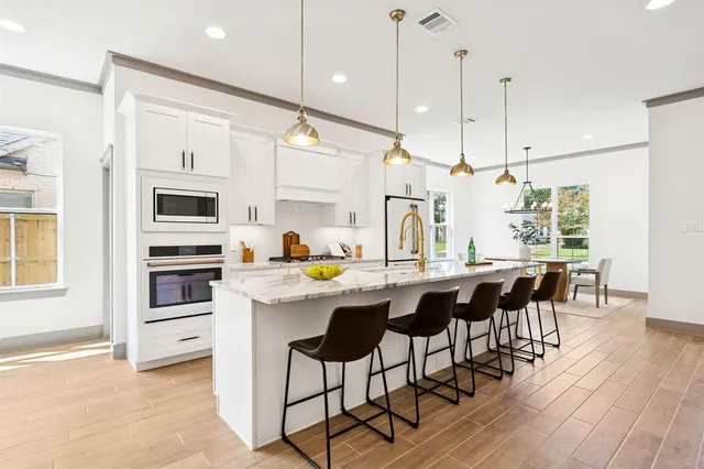 a kitchen with stainless steel appliances granite countertop a stove a refrigerator a kitchen island a sink and white cabinets with wooden floors