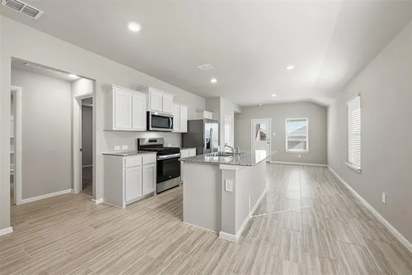 a kitchen with granite countertop a refrigerator oven a sink dishwasher and white cabinets with wooden floor