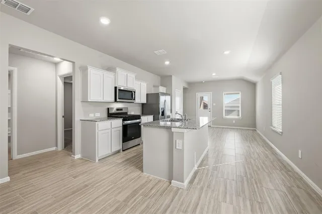 a kitchen with granite countertop a refrigerator oven a sink dishwasher and white cabinets with wooden floor