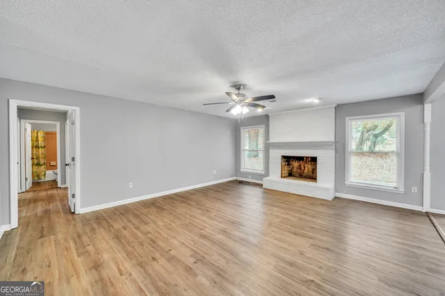 an empty room with wooden floor fireplace and windows