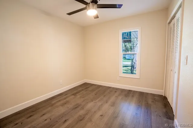 an empty room with wooden floor chandelier fan and windows