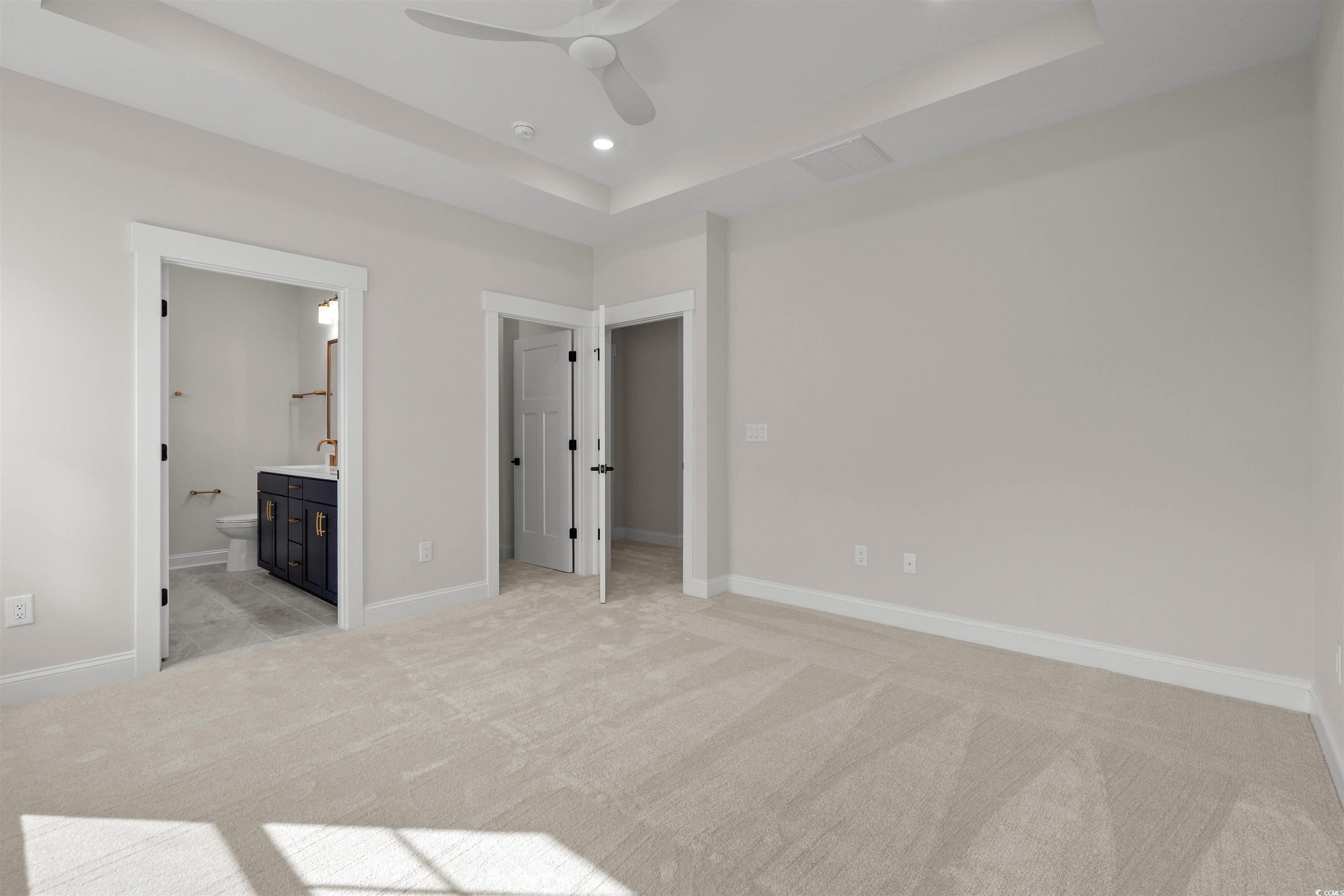 8476 Duke Place, Unit 32 Myrtle Beach, SC 29572 - Photo 26 of 40 Unfurnished bedroom featuring a raised ceiling, a walk in closet, light colored carpet, connected bathroom, and a ceiling fan