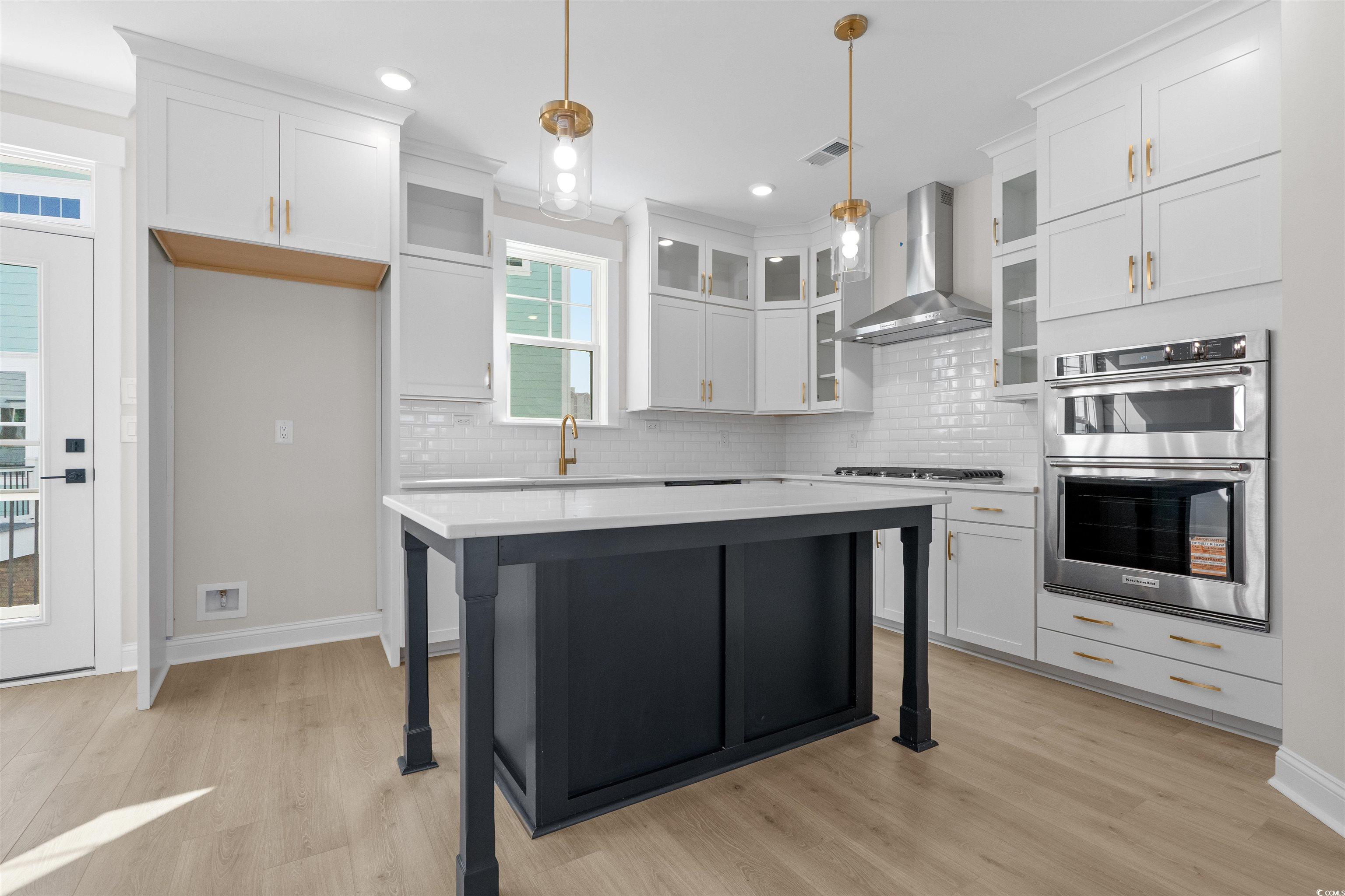 8476 Duke Place, Unit 32 Myrtle Beach, SC 29572 - Photo 7 of 40 Kitchen with wall chimney range hood, a breakfast bar area, double oven, glass insert cabinets, and a kitchen island