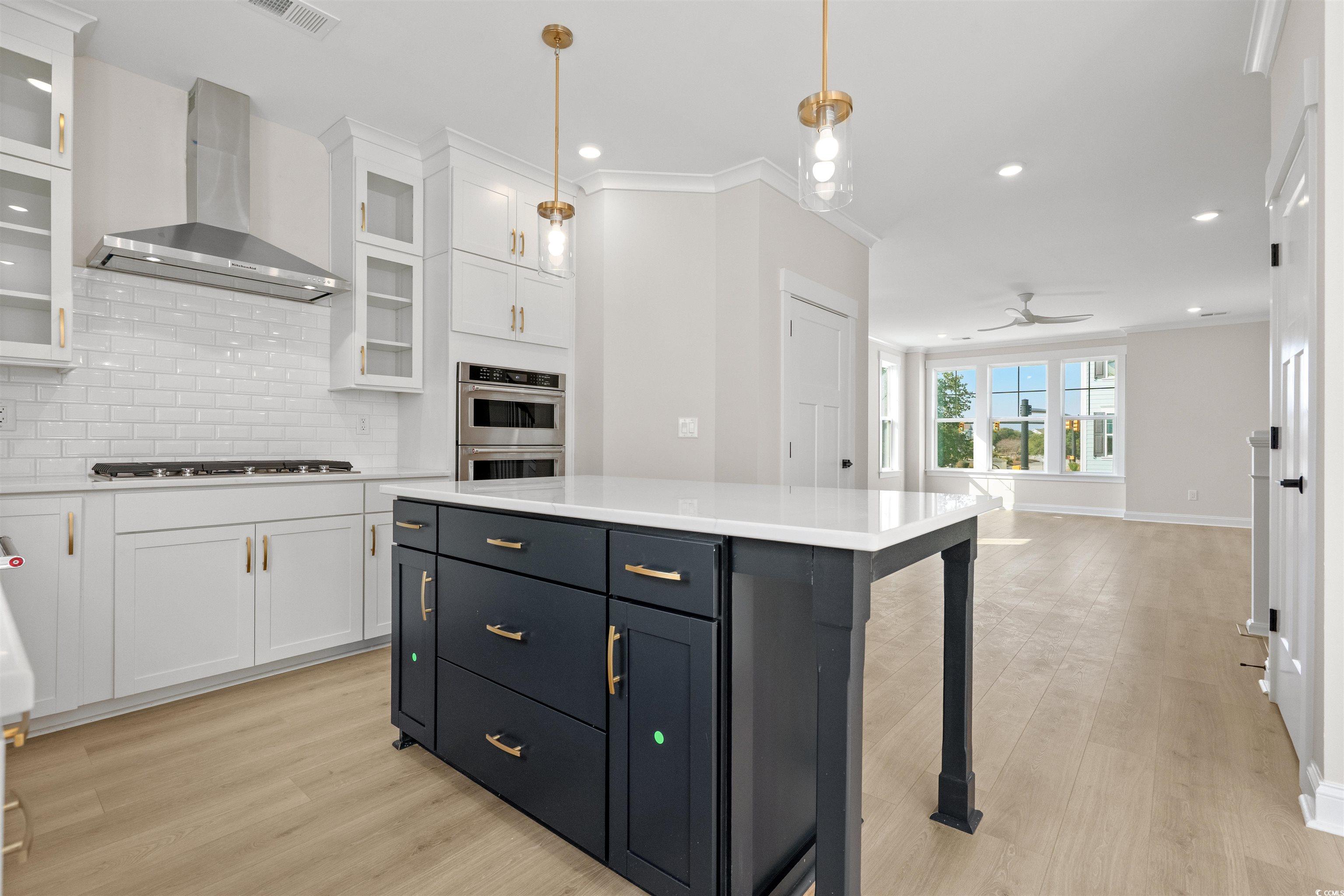 8476 Duke Place, Unit 32 Myrtle Beach, SC 29572 - Photo 9 of 40 Kitchen featuring white cabinetry, wall chimney exhaust hood, decorative backsplash, light wood finished floors, and crown molding