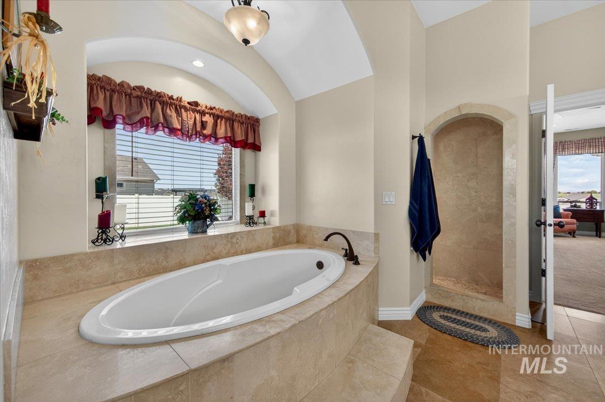 414 East Shafer View Drive Meridian, ID 83642 - Photo 22 of 50 Bathroom featuring an oval drop-in bathtub with tiled surround, a tiled walk-in shower with an arched entryway, and neutral-toned tiled flooring - Beautiful way to start & end your day!