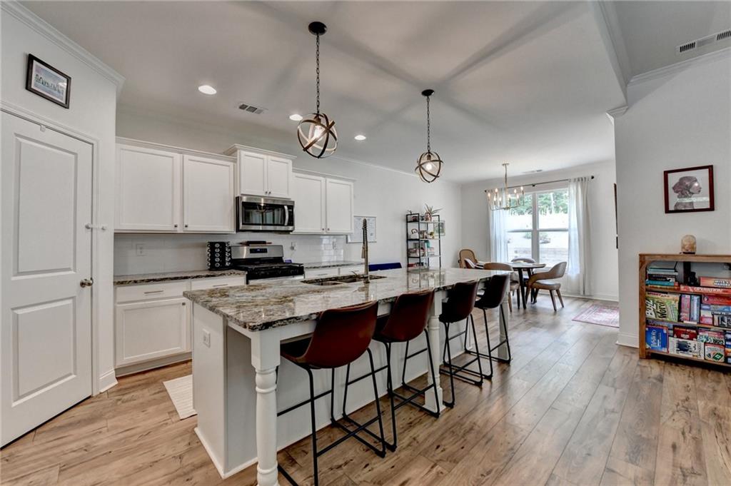 2129 Charmond Drive Monroe, GA 30656 - Photo 5 of 37 a kitchen with stainless steel appliances granite countertop a stove a refrigerator a microwave a dining table and chairs with wooden floor