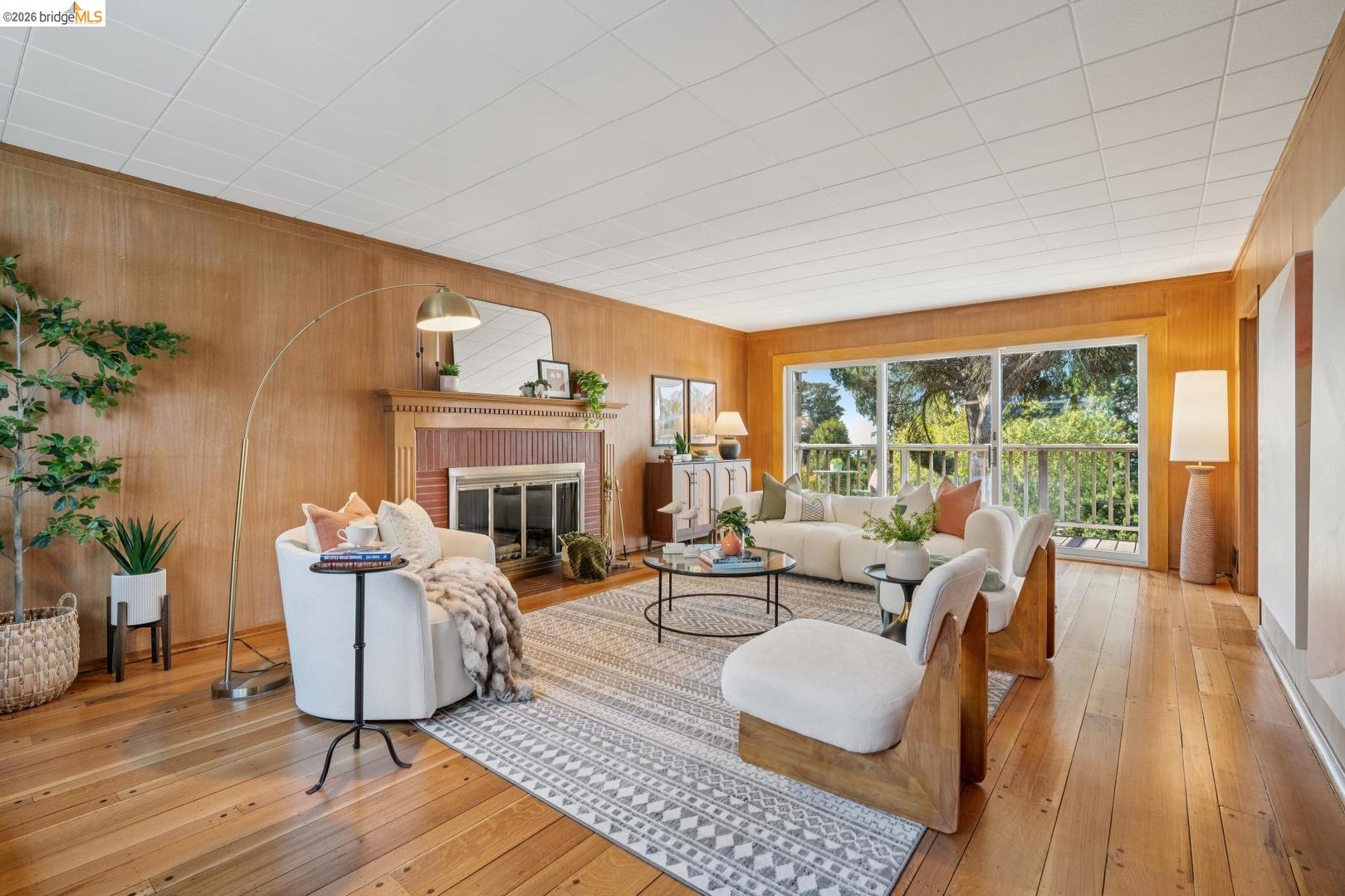155 Avenida Drive Berkeley, CA 94708 - Photo 5 of 86 Wood-finish flooring throughout, wood paneling, fireplace with brick surround and wood mantel, and sliding glass doors to outdoor balcony