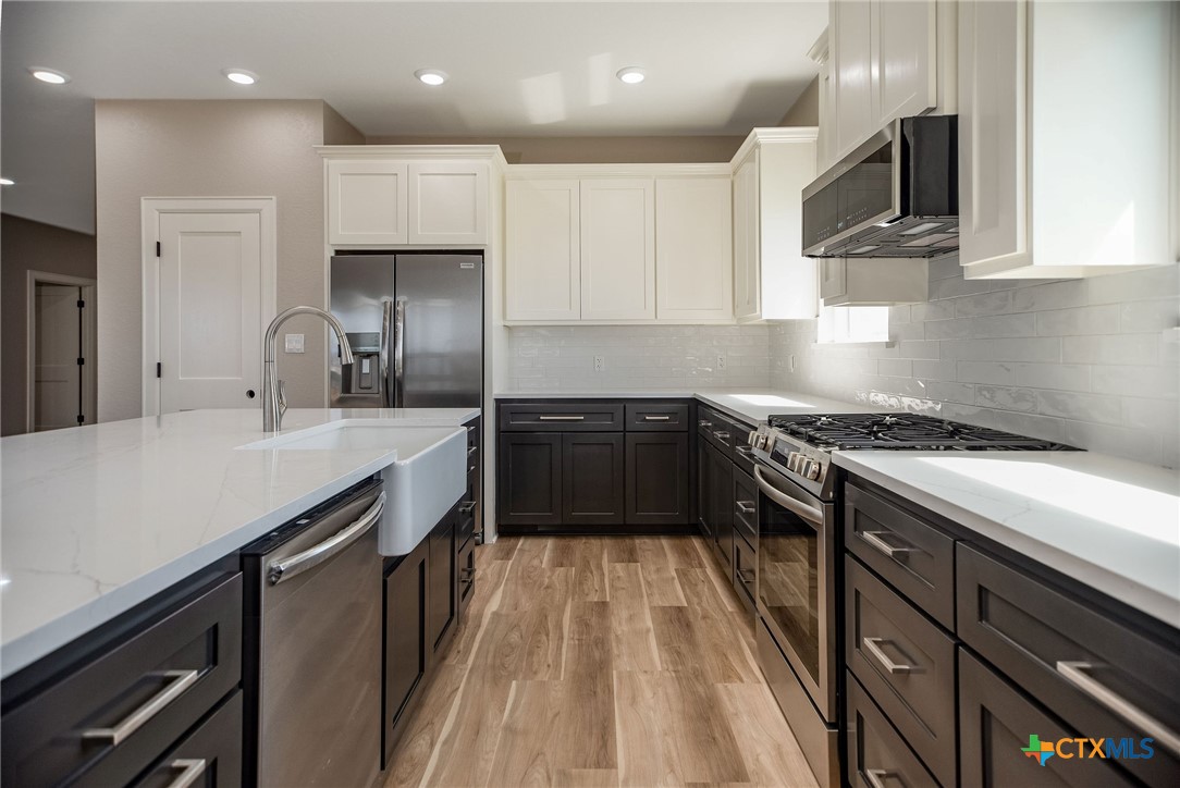 74 Whooping Crane Street Port O'Connor, TX 77982 - Photo 8 of 43 a kitchen with stainless steel appliances a sink dishwasher a stove top oven a refrigerator with wooden cabinets and floor