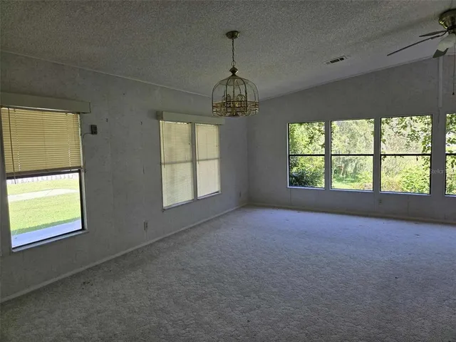 an empty room with windows chandelier and view of kitchen