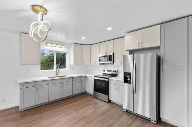 a kitchen with stainless steel appliances granite countertop a sink a stove a refrigerator and island with wooden floor