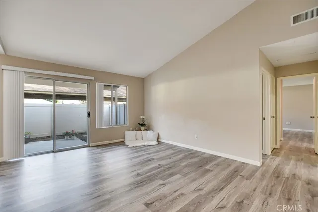 a view of an empty room with wooden floor and a kitchen