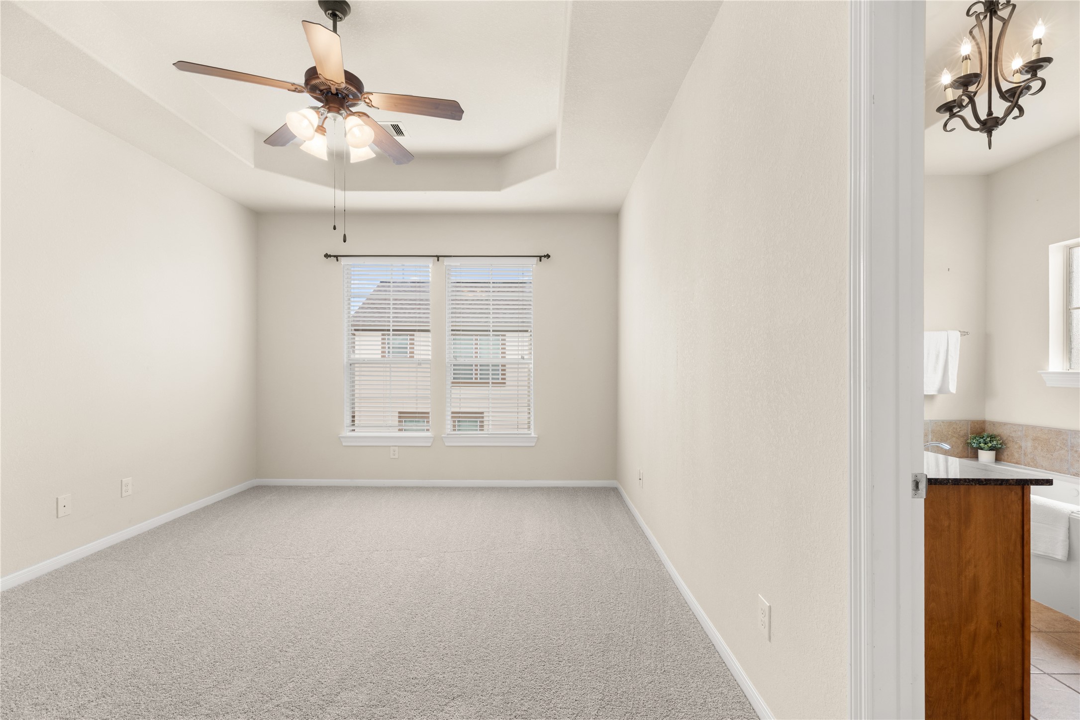 3334 Clearview Villa Way Houston, TX 77025 - Photo 14 of 35 This spacious, light-filled room features neutral walls and carpeting, a ceiling fan, and a view of the adjacent bathroom with a stylish chandelier and soaking tub. Ideal for relaxing after a long day.