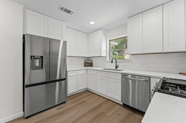 a kitchen with wooden floors white cabinets and stainless steel appliances