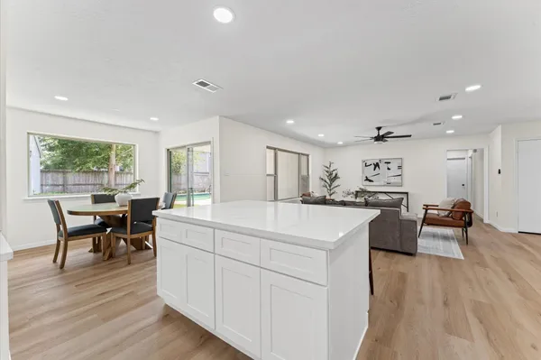 a large white kitchen with stainless steel appliances granite countertop a stove a sink a dining table and chairs with wooden floor