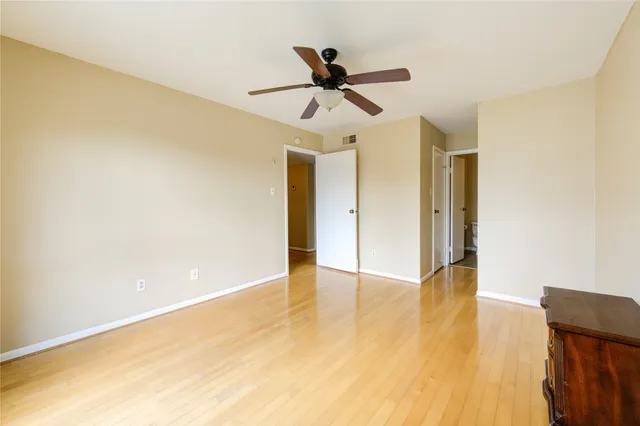 a view of an empty room with wooden floor and a ceiling fan