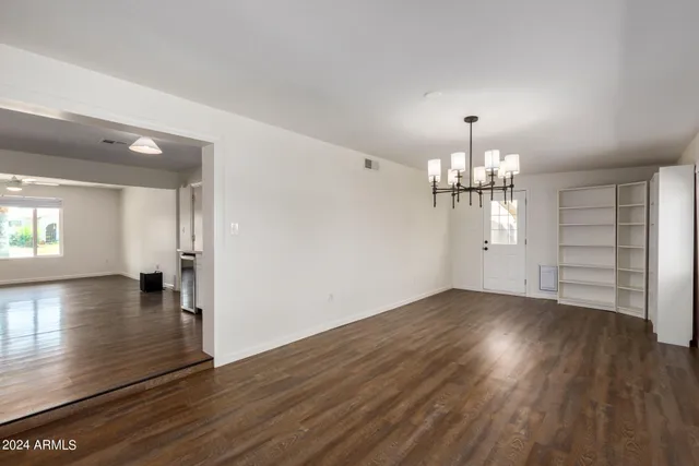 an empty room with wooden floor chandelier and window