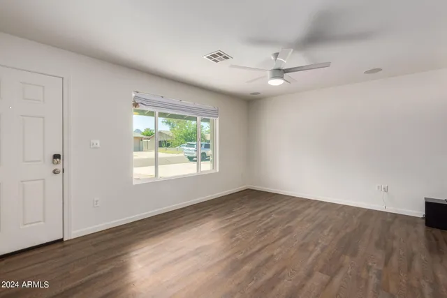 a view of an empty room with wooden floor and a kitchen