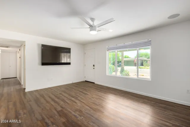 an empty room with wooden floor ceiling fan and windows