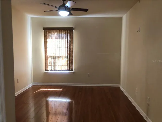 an empty room with wooden floor chandelier fan and windows