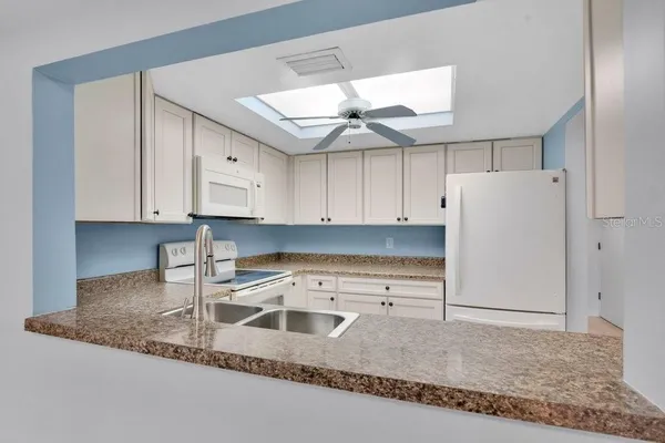 a kitchen with granite countertop a refrigerator a stove a sink and white cabinets