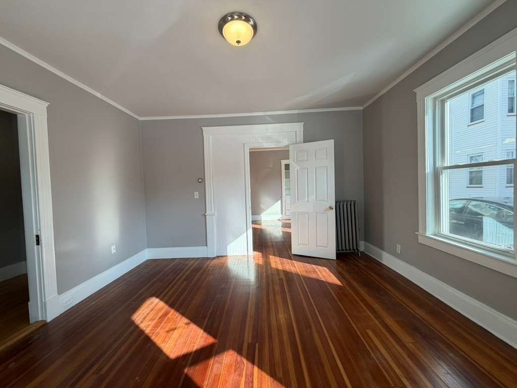 246 Rogers Street, Unit 1 Lowell, MA 01852 - Photo 3 of 17 a view of an empty room with wooden floor and a window
