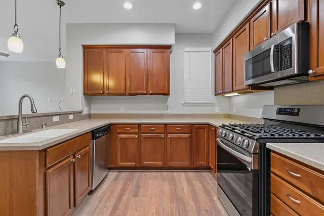 a kitchen with stainless steel appliances granite countertop wooden cabinets a stove top oven a sink and dishwasher with wooden floor