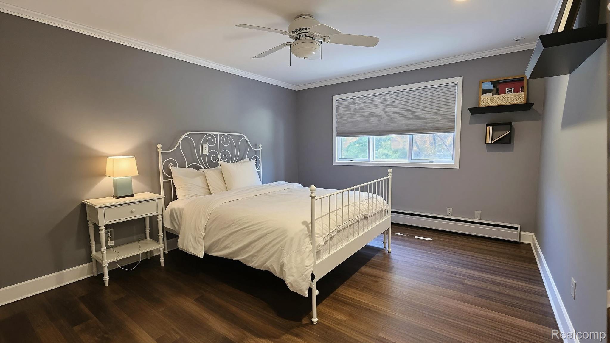 10202 Buhl Road Pinckney, MI 48169 - Photo 14 of 19 Bedroom featuring wood-finish flooring, a ceiling fan, crown molding, a window with a roller shade, and built-in shelving