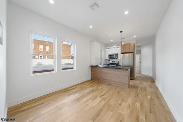 a view of kitchen with kitchen island stainless steel appliances wooden floor cabinets and a window