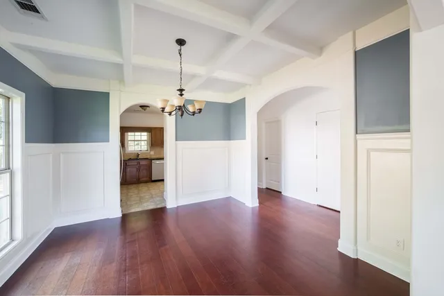 an empty room with wooden floor chandelier and windows