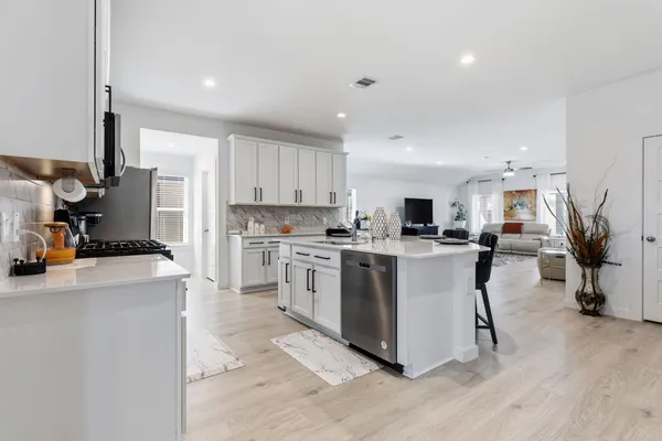 a kitchen with stainless steel appliances a sink a stove a refrigerator cabinets and a living room