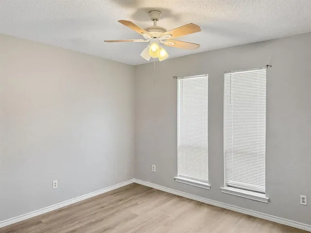 an empty room with wooden floor fan and windows