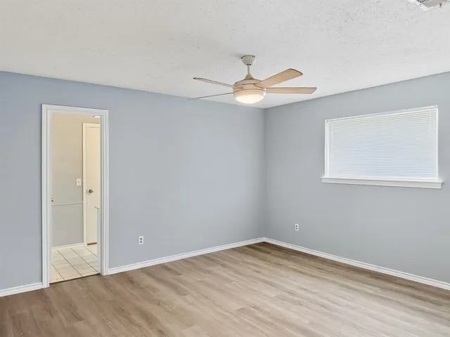 a view of an empty room with wooden floor and a ceiling fan