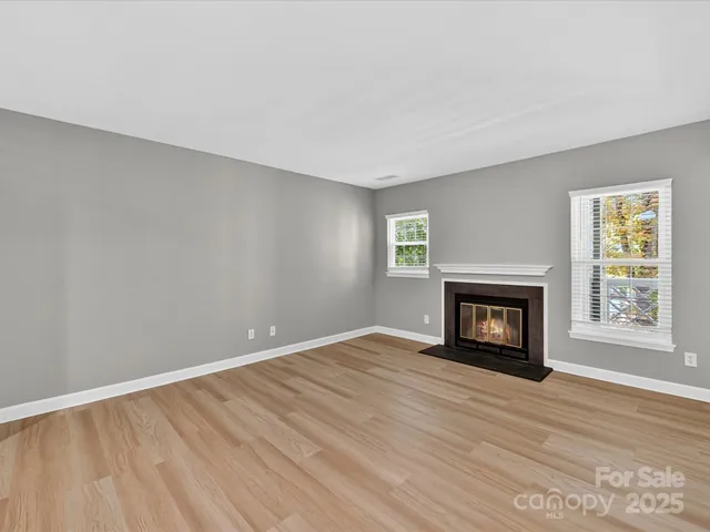 a view of an empty room with wooden floor fireplace and a window