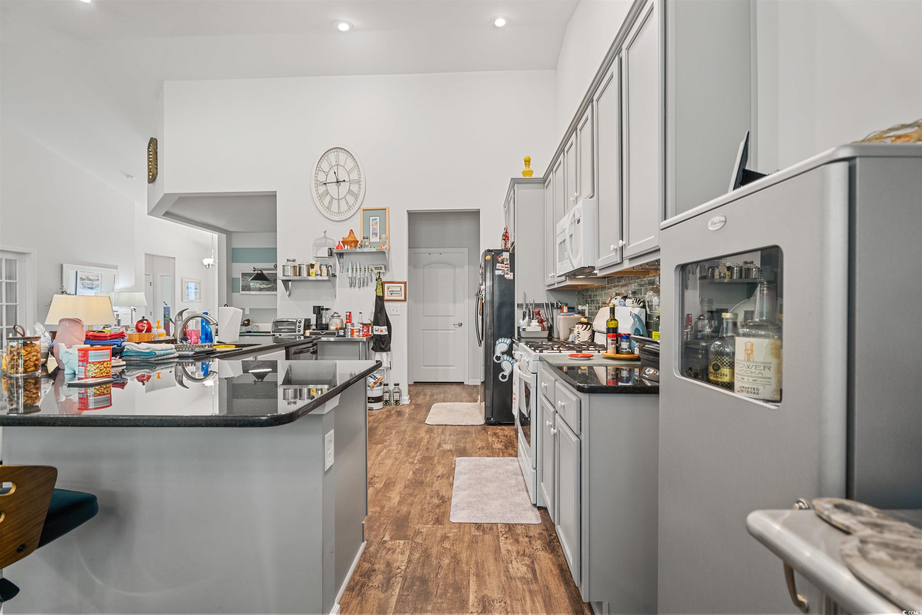 826 Cypress Way Little River, SC 29566 - Photo 13 of 40 Kitchen featuring white appliances, dark wood-style floors, dark stone counters, a kitchen bar, and gray cabinets