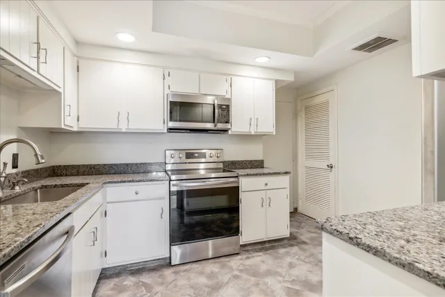 a kitchen with granite countertop white cabinets and stainless steel appliances