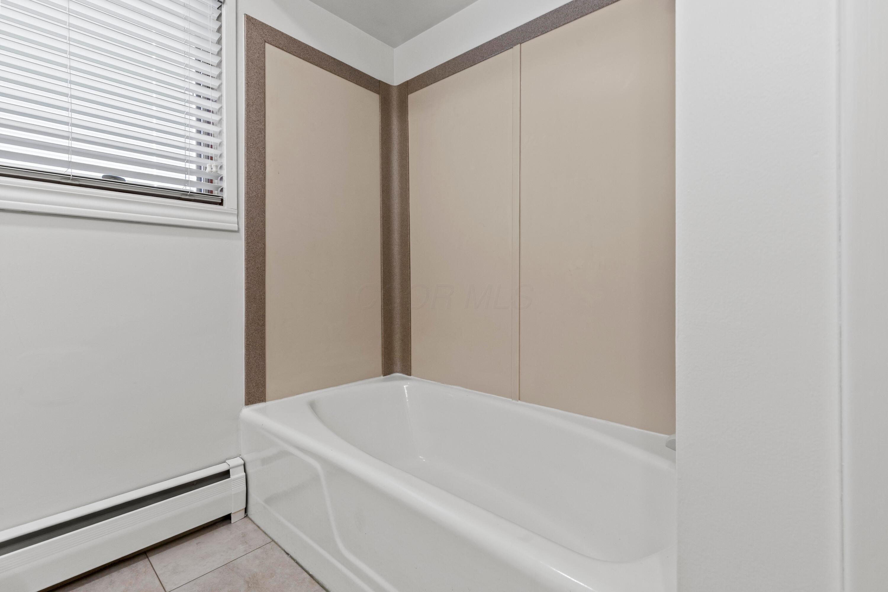 6982 Lee Road Westerville, OH 43081 - Photo 40 of 71 • New grouted vinyl flooring ~ 2024 • White painted walls • Tub/shower combination with corian surround • 4 bulb wall light • Linen closet with bi-fold doors