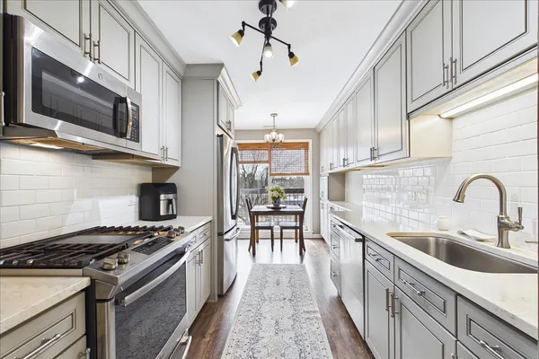 a kitchen with stainless steel appliances granite countertop a stove top oven a sink dishwasher a dining table and chairs with wooden floor