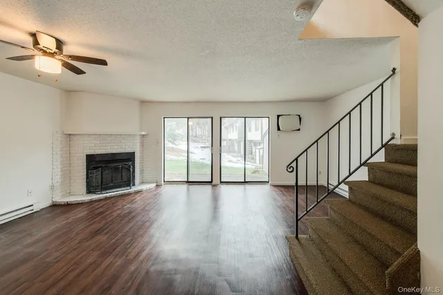 a view of an empty room with wooden floor fireplace and a window