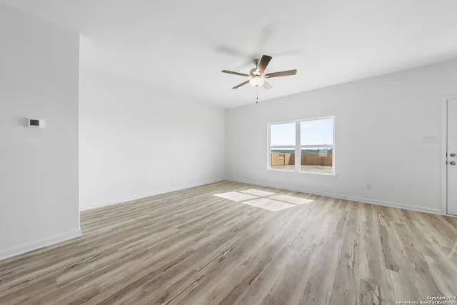 a view of empty room with wooden floor and fan