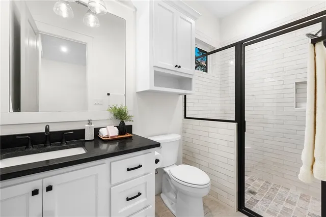 a bathroom with a granite countertop sink a toilet a mirror and shower