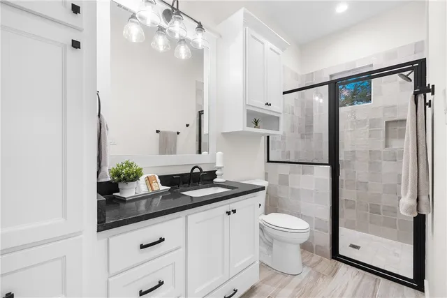 a bathroom with a granite countertop sink a toilet a mirror and shower